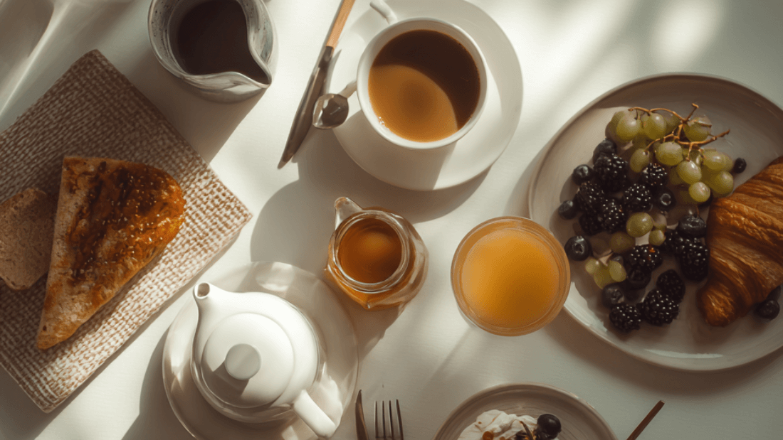 Calm morning flat lay with tea, coffee, fruit, yogurt, and soft sunlight on a breakfast table