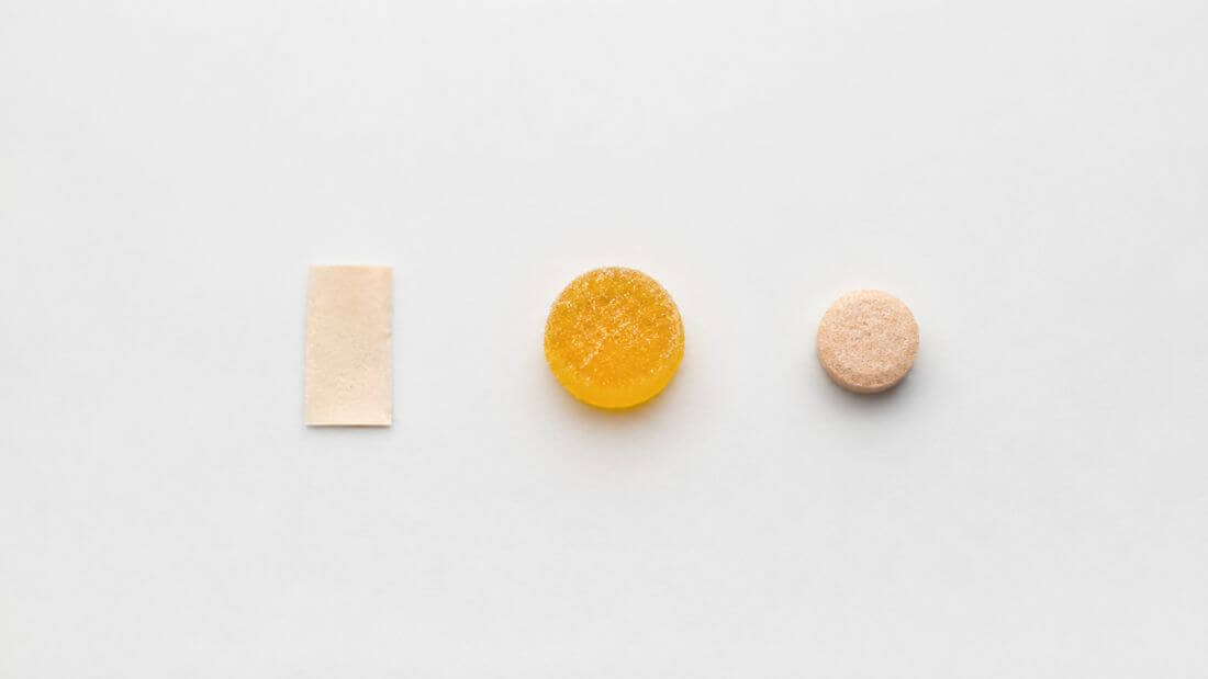 Flat lay of various supplement formats including a dissolving strip, a gummy, and a chewable tablet arranged neatly on a clean light surface  