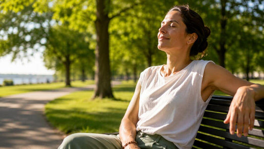  Person sitting outdoors in summer sunlight on a park bench, relaxed and enjoying fresh air with greenery in the background 